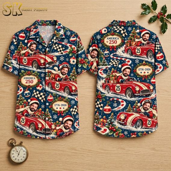 Both sides of a dark blue short-sleeve button-up shirt shown flat on a hanger, featuring a repeating pattern of a Santa-hatted vintage race car driver, checkered flags, Christmas trees, and oval plaques reading 'America 250' and '1776–2026'.