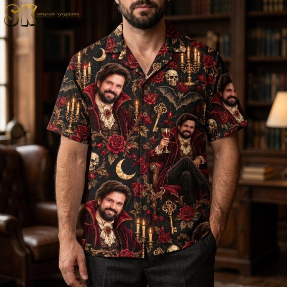 A man wearing a black short-sleeve button-up shirt featuring an all-over print of a Victorian vampire seated in an armchair with gold candelabras and red roses throughout the design.