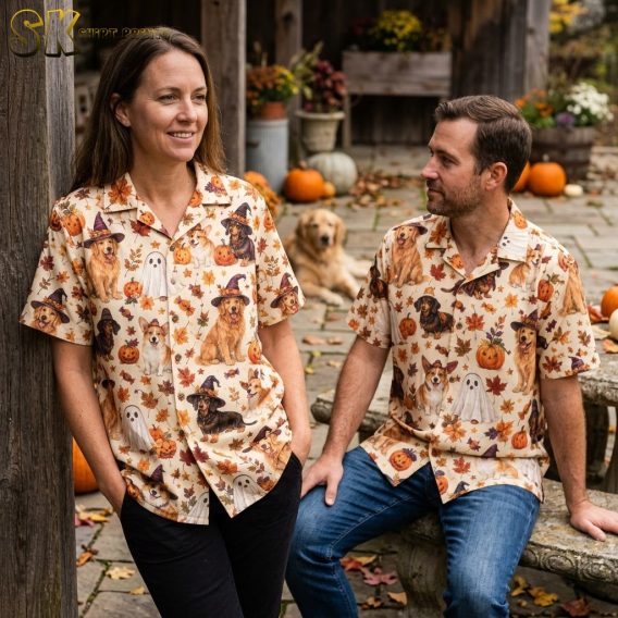Couple wearing matching cream halloween hawaiian shirts covered in witch-hat dogs, ghost-costume dogs, pumpkins, and fall leaves.