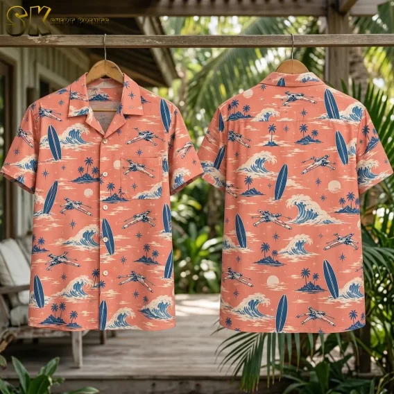 Two coral pink shirts hang from a wooden rail, showing front and back spacecraft-and-surf prints amid tropical greenery.