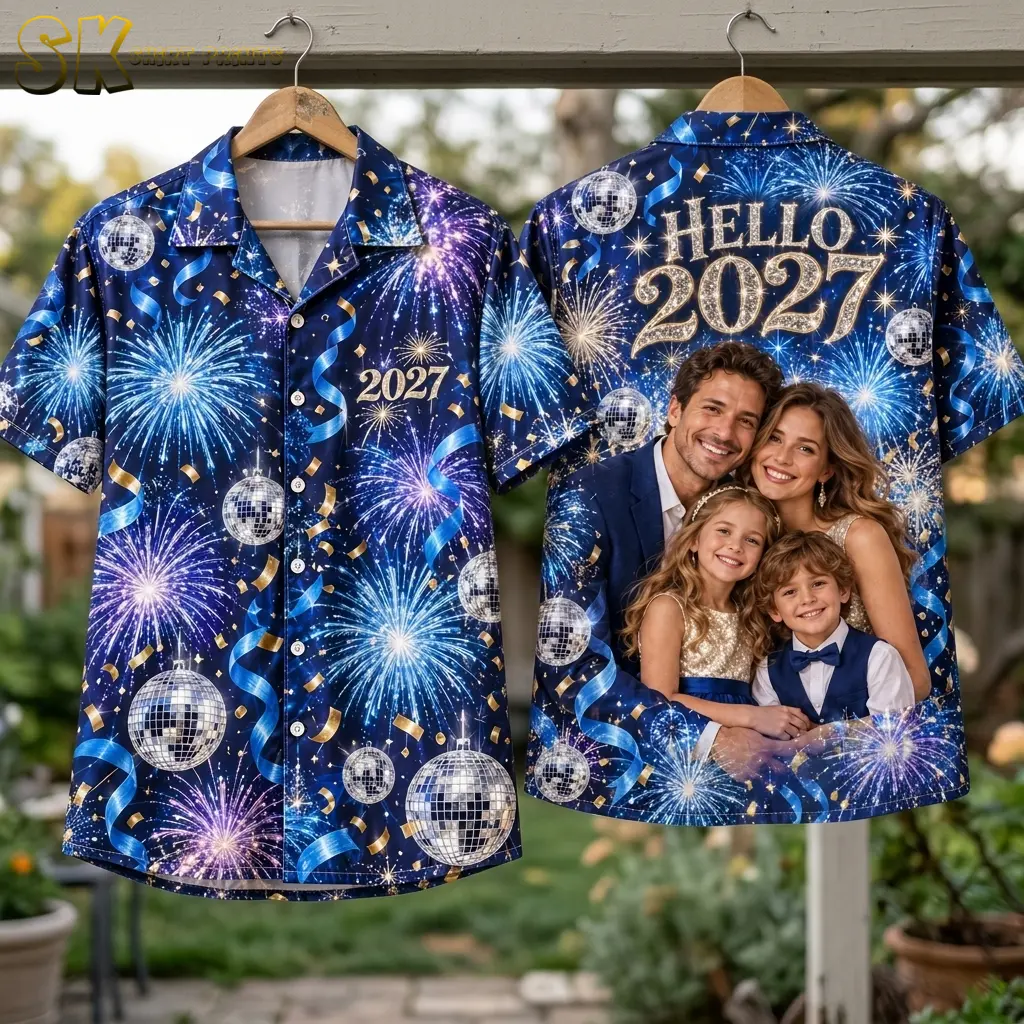 Front and back displays of the navy fireworks shirt hang outdoors on wooden hangers, revealing “HELLO 2027” above a printed family portrait.