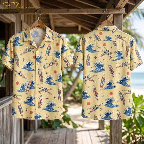 Front and back shirts hang from wooden hangers on a beachside porch, displaying the pale yellow wave, surfboard, and spacecraft print.