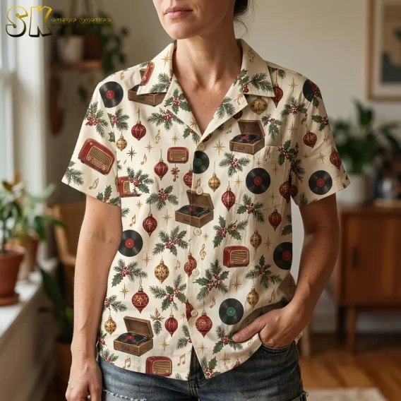 A woman wearing a hawaiian christmas shirt womens style stands in a plant-filled room, with the open camp collar, button placket, and detailed record player and ornament motifs visible up close.