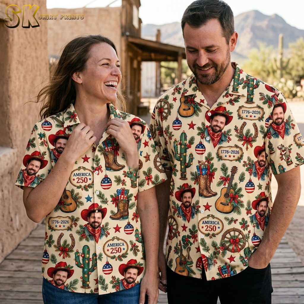 A smiling woman and man stand side by side outdoors, both wearing the same cream shirt printed with cowboy portraits, guitars, cacti, and 1776–2026 text plaques, with a desert landscape visible behind them.