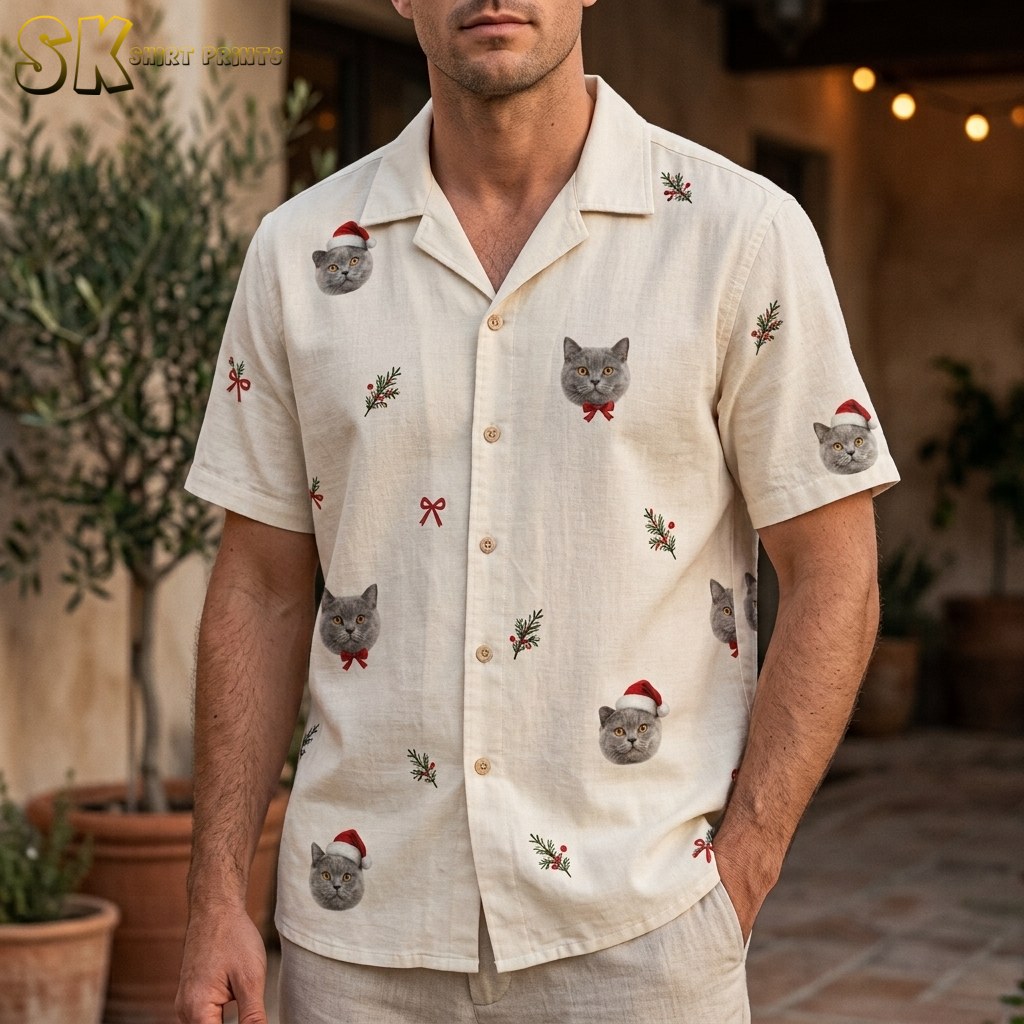 A man stands outdoors wearing a cream hawaiian shirt mens christmas santa claus party aloha holiday beach style, with gray cat faces in Santa hats and red bow ties clearly visible across the chest and sleeve.