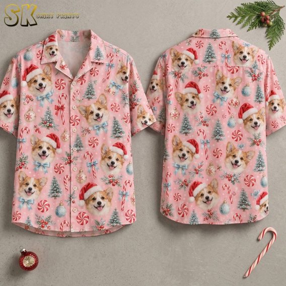 Front and back of a pink short-sleeve button-up shirt displayed on invisible hangers, showing an all-over pattern of corgi faces in Santa hats, candy canes, frosted Christmas trees, and ornaments.