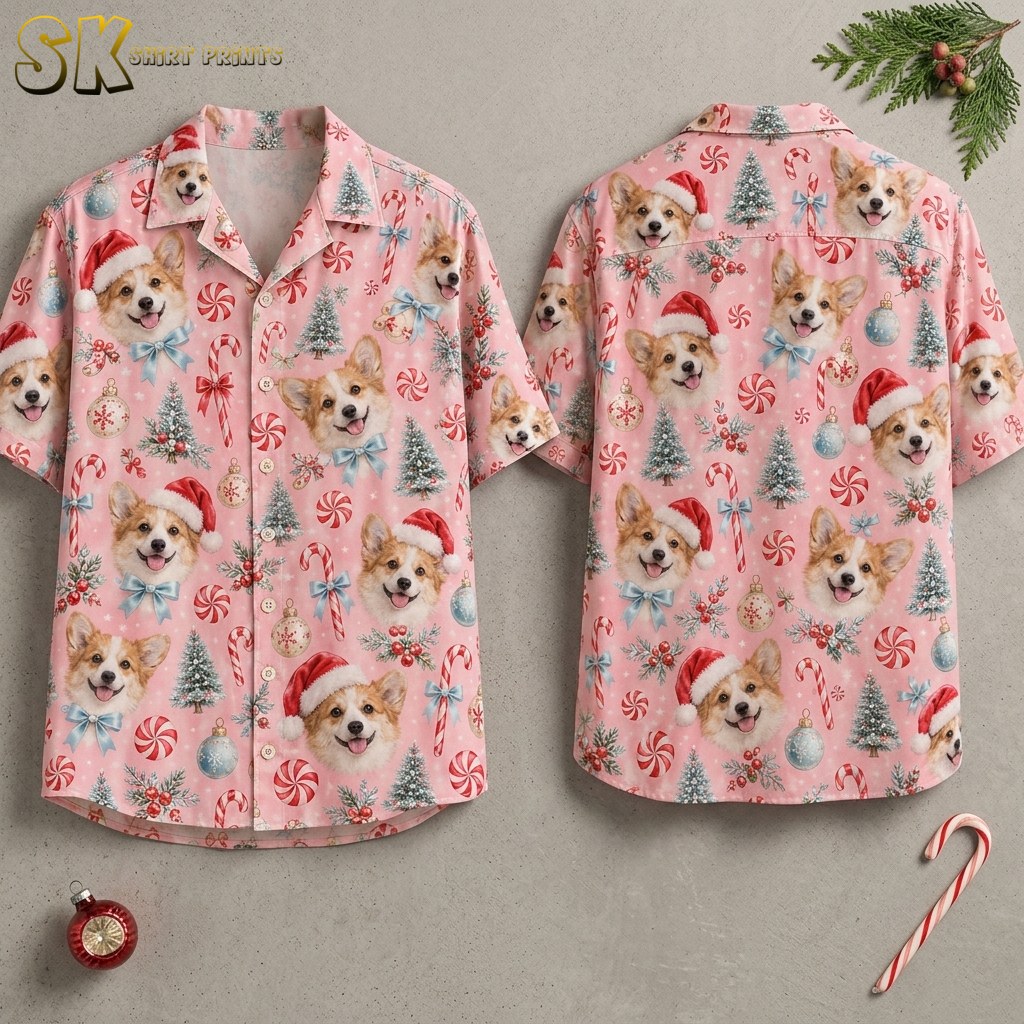 Front and back of a pink short-sleeve button-up shirt displayed on invisible hangers, showing an all-over pattern of corgi faces in Santa hats, candy canes, frosted Christmas trees, and ornaments.