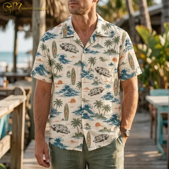 A man wears a cream Star Wars Hawaiian shirt with spacecraft and wave motifs on a wooden walkway near the beach.