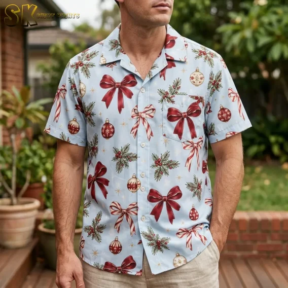 A man wears a light blue Christmas Hawaiian shirt with large red bows and patterned baubles on a wooden deck.