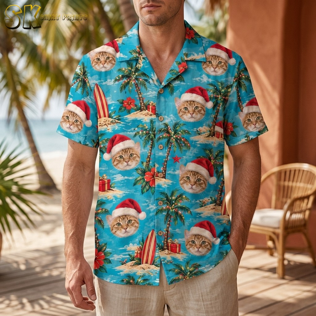 A man wearing a santa aloha shirt stands on a beach-side deck, the turquoise fabric covered in orange tabby cat faces under red Santa hats alongside palm trees and wrapped gifts.