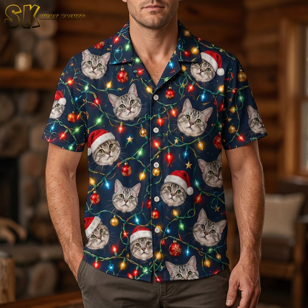 A man wearing a funny christmas hawaiian shirt printed with photorealistic cat faces in Santa hats and glowing multicolored string lights on a navy background, photographed from the chest down in a warm wood-paneled interior.