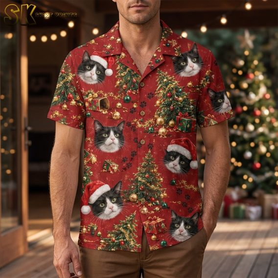 A man wearing a christmas hawaiian shirt for men stands outdoors near a decorated Christmas tree, with large tuxedo cat faces and Santa hats clearly visible across the front of the red shirt.