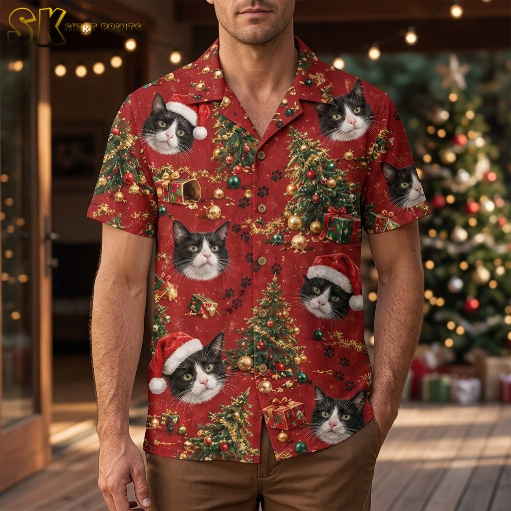 A man wearing a christmas hawaiian shirt for men stands outdoors near a decorated Christmas tree, with large tuxedo cat faces and Santa hats clearly visible across the front of the red shirt.