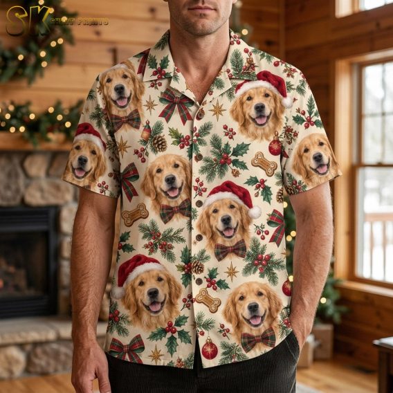A man wearing christmas hawaiian shirts for men stands in a warmly lit wood-paneled room with a decorated fireplace behind him, the Golden Retriever faces with Santa hats clearly visible across the chest.