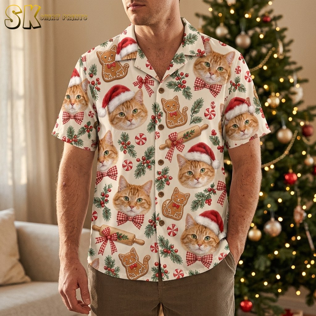 A man wearing a christmas hawaiian shirt mens style button-up covered in orange tabby cat faces with Santa hats and red gingham bows, standing in front of a decorated Christmas tree.