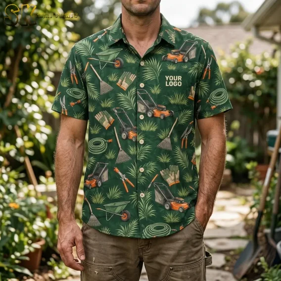 A man standing in a lush backyard garden wearing a dark green custom Hawaiian shirt with your logo printed on the left chest, surrounded by orange lawn mower and garden tool motifs across the fabric.