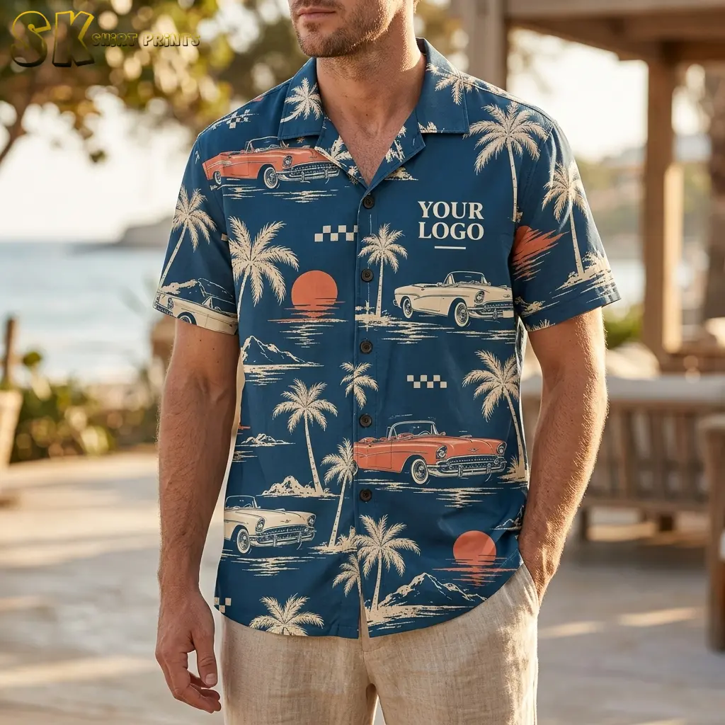 A man wearing a teal logo Hawaiian shirt stands at an outdoor patio with the ocean visible behind him, the vintage car and palm tree print clearly spread across the chest.