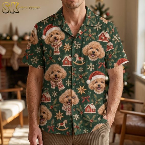A man wearing a mens christmas hawaiian shirt covered in illustrated poodle faces, some in Santa hats, stands in a warmly decorated living room with a lit fireplace and Christmas tree behind him.