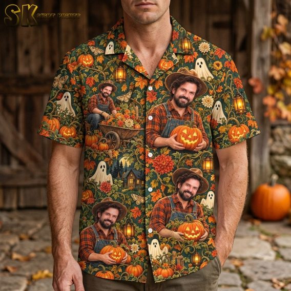 A man wearing a mens halloween hawaiian shirt stands outdoors in front of a rustic barn, with the chest print of the smiling farmer holding a jack-o'-lantern clearly visible at center front.
