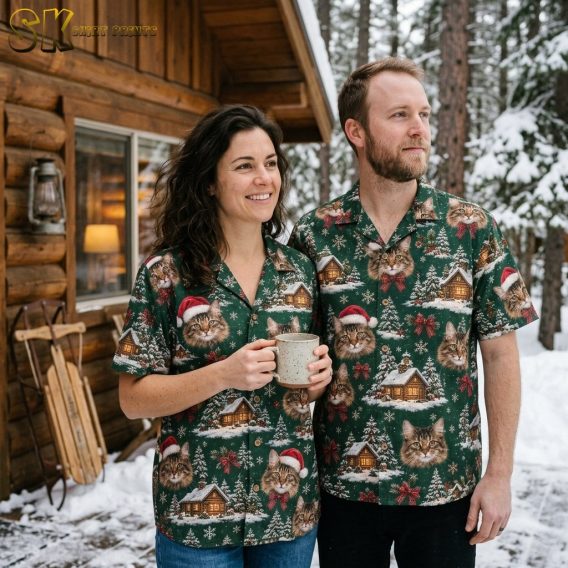 A smiling woman holding a mug and a man stand together outside a snow-covered log cabin, both wearing matching christmas hawaiian shirts printed with tabby cats in Santa hats and red plaid bows on a deep green background.