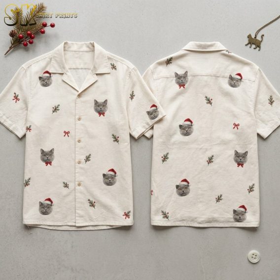 Both sides of a cream mens christmas aloha shirt laid flat, showing repeated gray cat faces in Santa hats and bow ties alongside holly sprigs and red bows on the front and back panels.