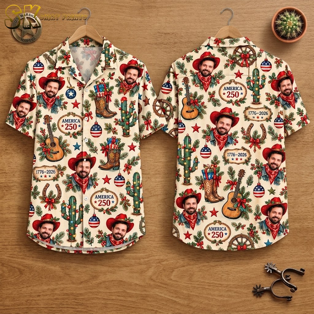 Front and back of a cream short-sleeve button-up shirt hanging on wooden hangers, showing an all-over pattern of a smiling cowboy portrait, decorated boots, cacti, guitars, and America 250 commemorative plaques.