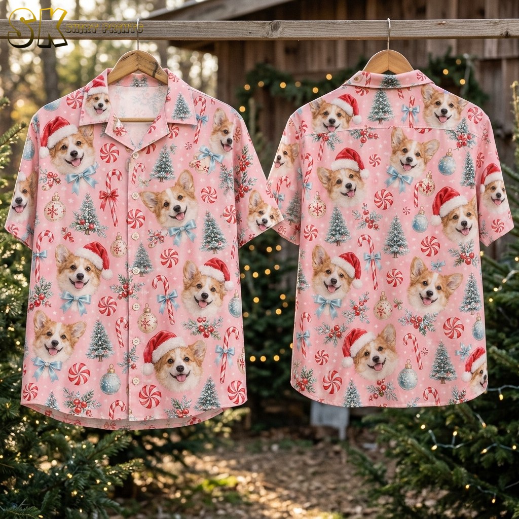 Front and back of the pink corgi Santa shirt hang on wooden hangers outdoors among evergreen trees strung with warm lights, showing the full repeat of dog faces, ornaments, and candy canes on both sides.