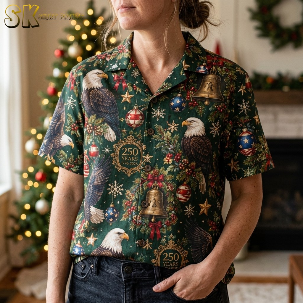 A close-up view of a woman wearing the dark green short-sleeve shirt, highlighting the detailed illustration of bald eagles alongside gold bells, red-berried pine branches, and star-and-stripe baubles in the pattern.
