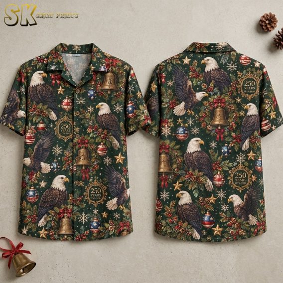 Front and back hanger view of a dark green short-sleeve button-up shirt covered in an all-over pattern of realistic bald eagles, Christmas bells with red bows, star-and-stripe baubles, pine branches, and circular badges reading 250 YEARS 1776-2026.