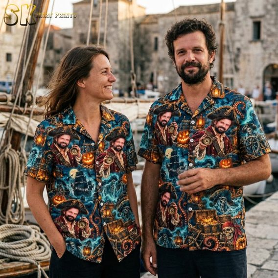 A couple shown together, with one person wearing the dark blue pirate Halloween aloha shirt covered in repeated pirate portraits, treasure chests, and jack-o'-lanterns.