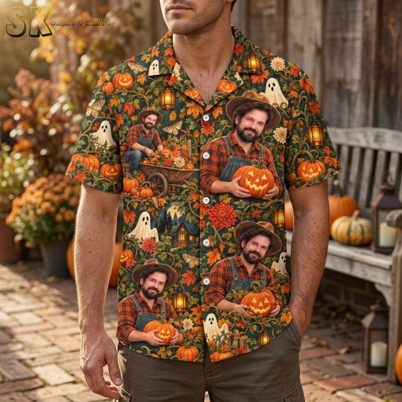 A man wearing the dark green halloween hawaiian shirt, which features large portraits of a man holding a carved pumpkin alongside ghost figures and autumn foliage across the fabric.