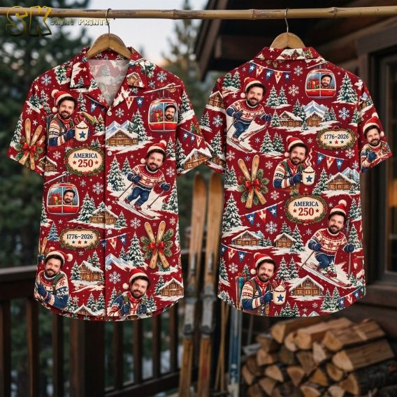 The shirt hangs on a bamboo rod outdoors with both the front and back visible, showing the full all-over pattern of skiing figures, snow-covered cabins, evergreen trees, and the 1776-2026 plaque against a deep-red background.
