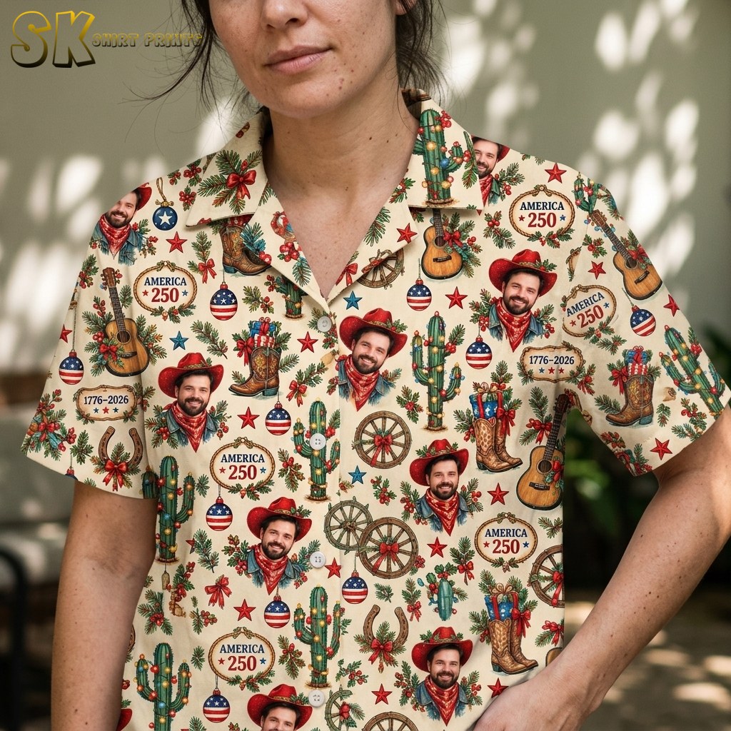 A woman wears the cream western holiday shirt in a shaded outdoor spot, and the close-up framing brings out the fine detail on the cowboy portraits, wagon wheels, horseshoes, and America 250 badge graphics.