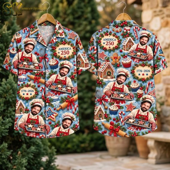 The shirt hangs on two wooden hangers outdoors against green foliage, showing the front with the smiling chef and 'AMERICA 250' wreath and the back with the gingerbread house centerpiece and '1776–2026' text.