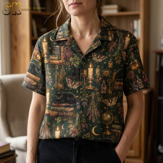 Close-up of a woman wearing a dark green spooky hawaiian shirt, showing detailed illustrations of black cats, antique books, candles, moths, and ornate keys.
