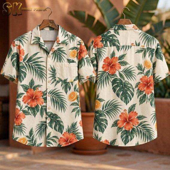 Front and back of the cream tropical shirt hanging on wooden hangers indoors, showing the hibiscus flowers, monstera leaves, and orange fruit slices printed across the full surface of both sides.