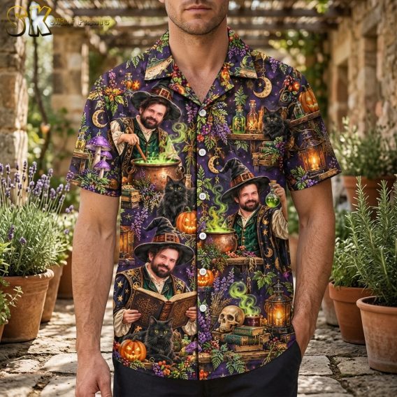 A man wearing a dark purple short-sleeve button-up shirt printed with a repeating pattern of a bearded wizard, black cats, pumpkins, and glowing cauldrons.