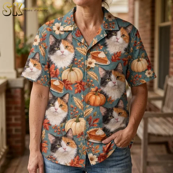 A woman wears a blue short-sleeve shirt with large calico cat faces and pumpkin pie illustrations, paired with jeans on a porch.