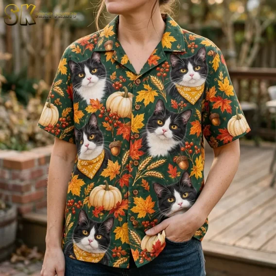 A woman wears a green short-sleeve shirt with tuxedo cat faces, yellow bandanas, and fall leaves, paired with blue jeans.