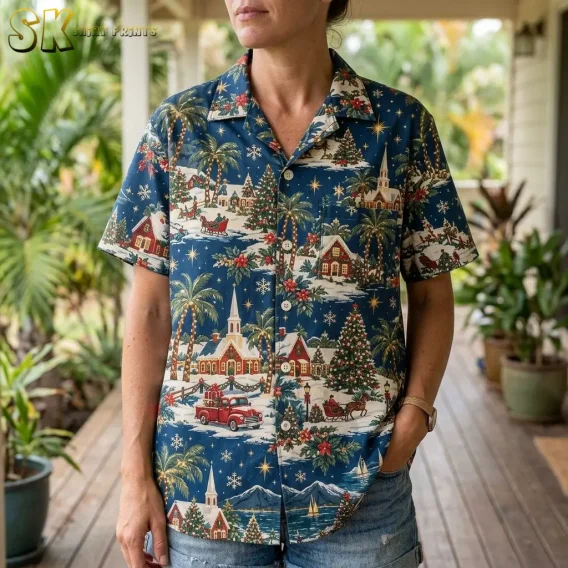 A woman standing on a covered porch wearing a hawaiian christmas shirt womens style, with the palm-lined village scene, red truck, and horse-drawn sleigh motifs filling the front panel.