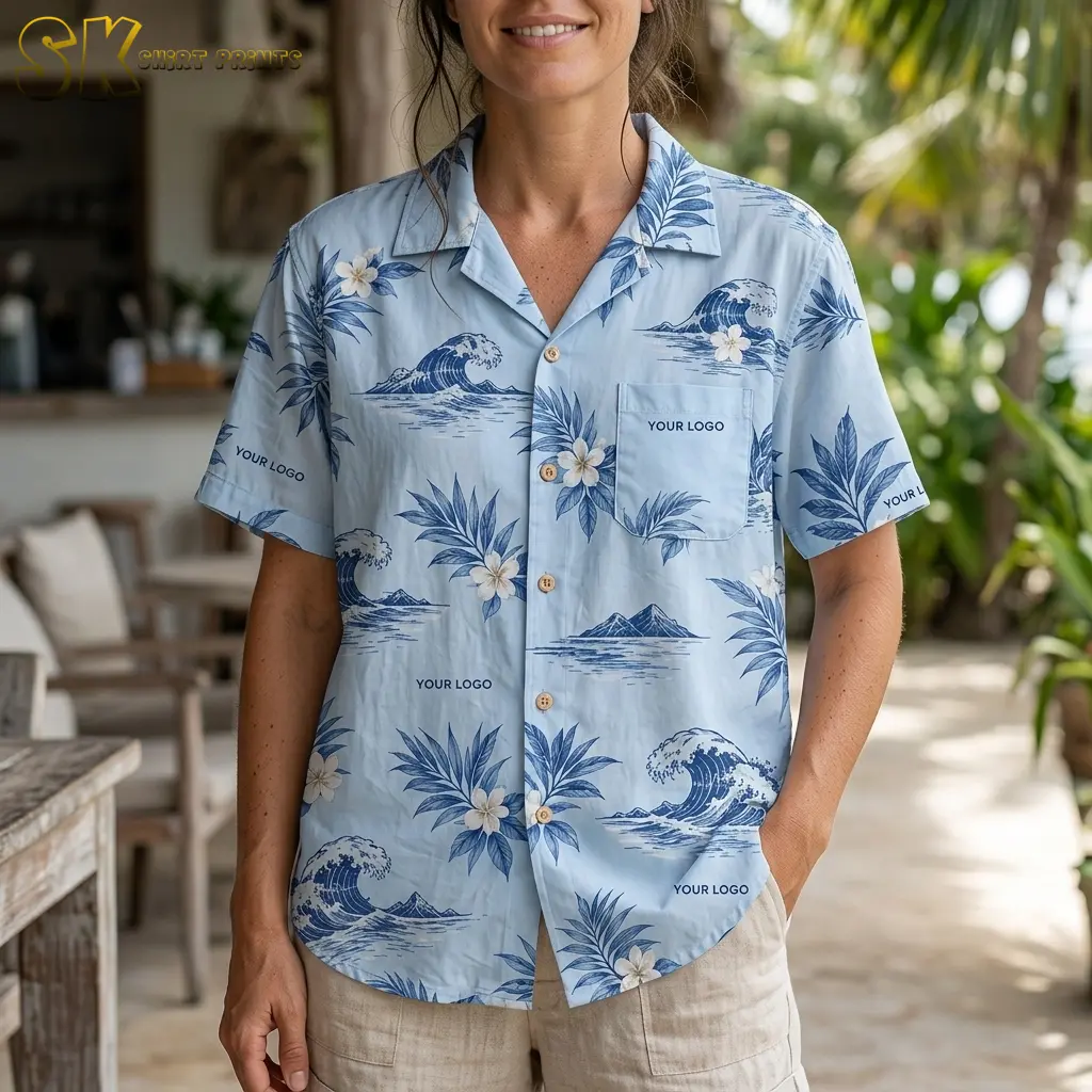 A woman smiles while wearing the light blue Hawaiian shirt in a tropical garden setting, with the white plumeria flowers and dark blue wave motifs on the chest and sleeves shown in close detail.