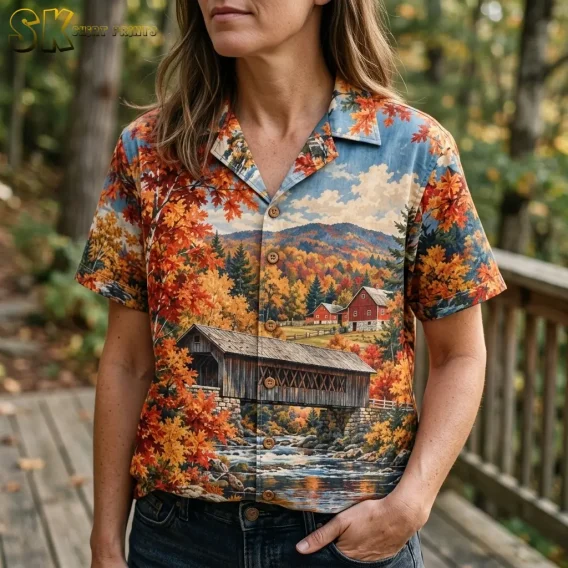 A woman wears an autumn landscape shirt with jeans, showing the collar, front buttons, and detailed covered bridge print.