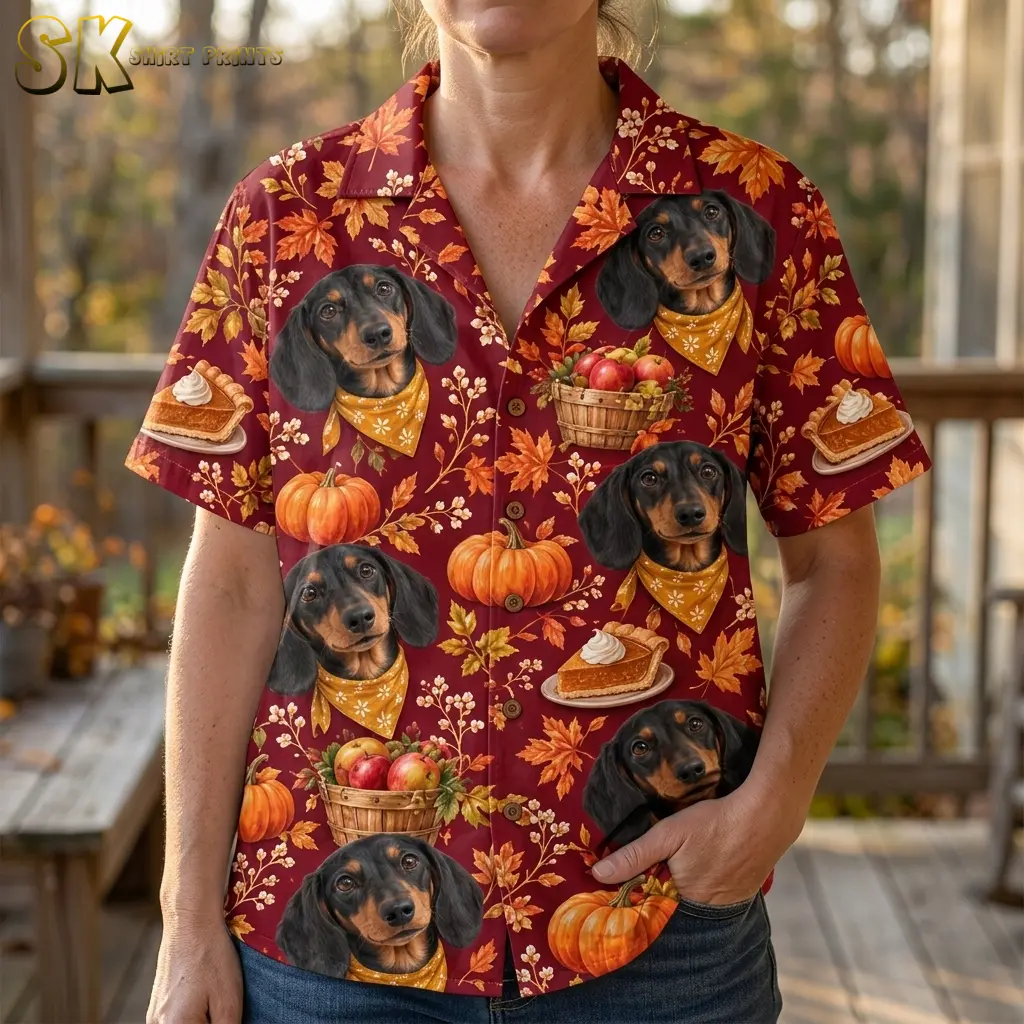 A woman wears a maroon short-sleeve shirt with bandana-wearing dachshunds and pumpkin pie illustrations, with one hand in her jeans pocket.