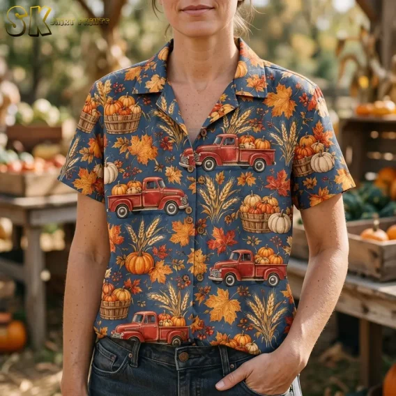 A woman wears a blue-gray harvest shirt tucked into jeans, with pumpkin baskets and red trucks visible across the front.