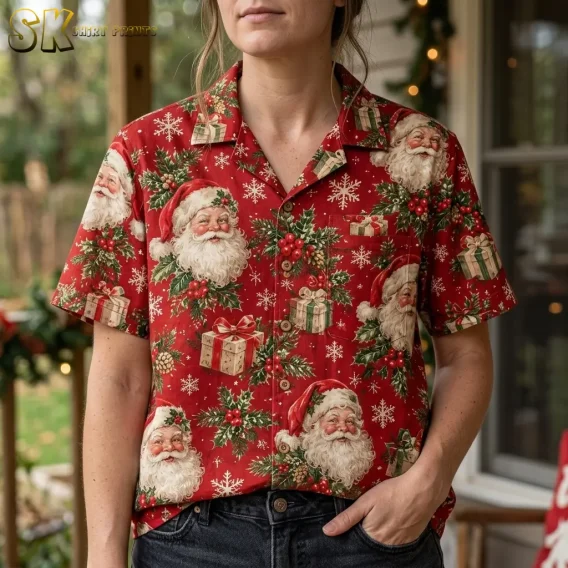 A woman wears a red Christmas themed Hawaiian shirt with Santa portraits and holly, with one hand in her dark jeans pocket.