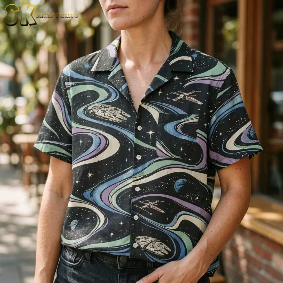 A woman wears a black Star Wars Hawaiian button-up shirt with dark jeans, showing the camp collar, chest pocket, and spacecraft print up close.
