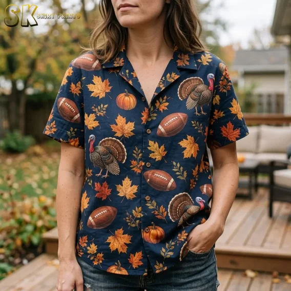 A woman wears a navy Thanksgiving button-up shirt with large turkey illustrations and orange leaves, keeping one hand in her jeans pocket.