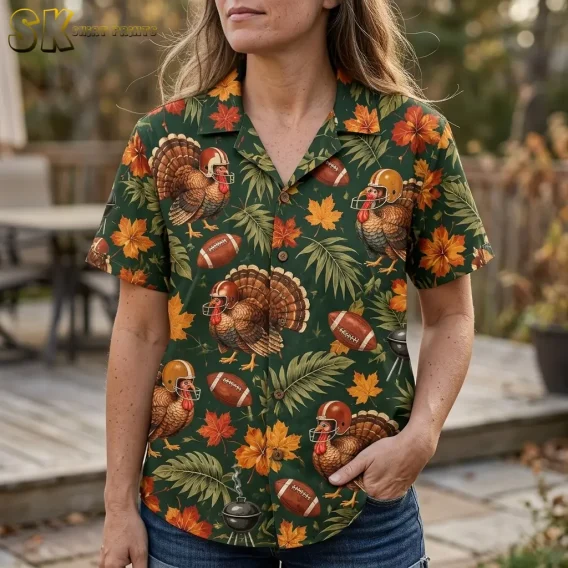 A woman wears a green Thanksgiving button up shirt with helmeted turkeys and orange leaves, paired with denim shorts outdoors.
