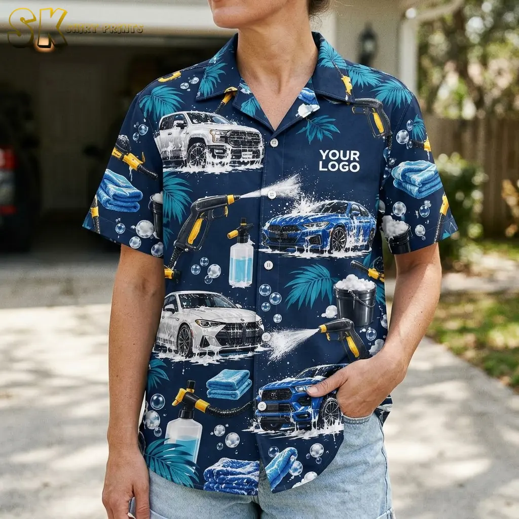 A woman wearing the navy car wash shirt stands in a residential driveway, showing the front panel detail of soapy sedans, foam spray guns, blue microfiber towels, and a soap bottle against the dark navy base.