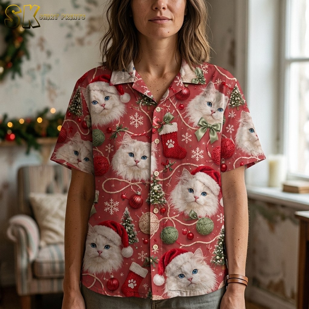 A woman's torso shot indoors shows the red shirt's pattern up close, with oversized fluffy cat faces, a paw-print Christmas stocking, green yarn balls, and a satin bow all legible at this scale.